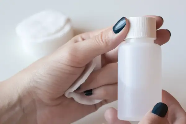 Ellerinde pamukla beyaz bir plastik şişe tutan kişi.