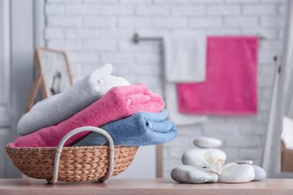Düzgünce katlanmış renkli havluların bir sepet içinde olduğu, taşlar ve bir çiçekle süslenmiş banyo ortamı.