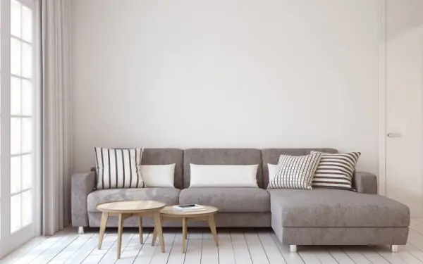 Minimalist tasarımlı bir oturma odası, gri kanepe ve dekoratif yastıklar, ahşap kahve masaları.