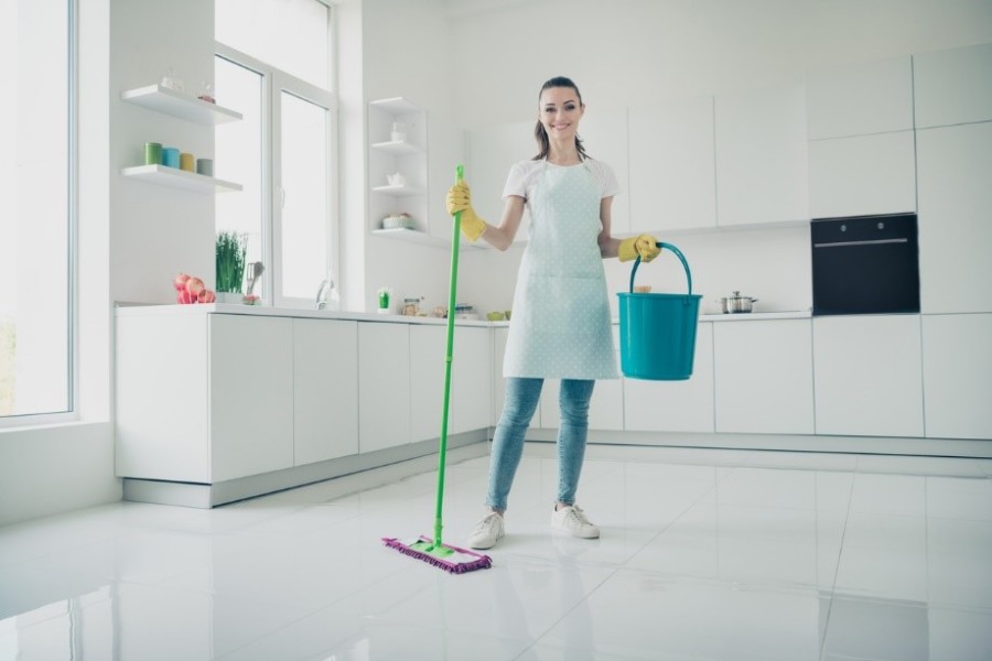 Beyaz modern bir mutfakta temizlik yapmakta olan önlüklü kadın.