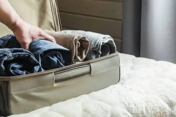 Bir kişi, bavula katlanmış kot pantolonlar yerleştiriyor.