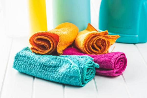 Renkli mikrofiber temizlik bezleri ve arka planda temizlik ürünlerinin şişeleri.