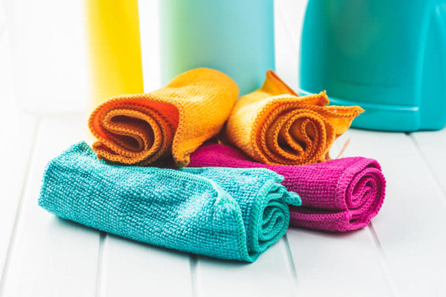 Renkli mikrofiber temizlik bezleri ve arka planda temizlik ürünlerinin şişeleri.