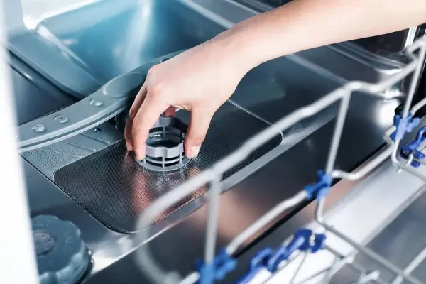 Bulaşık makinesinin alt sepetine deterjan kapsülü bölmesinin kapağını yerleştiren bir el.