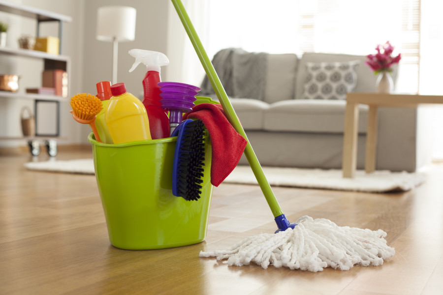 Temizlik malzemeleri dolu yeşil kova ve yerde mop, arka planda oturma odası.