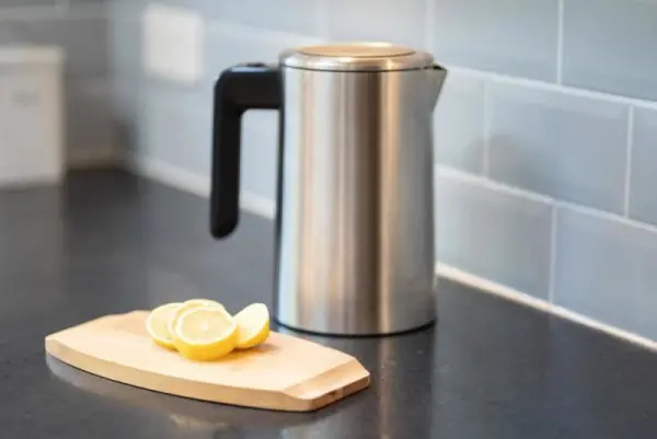 Mutfak tezgahı üzerinde kesilmiş limon dilimleri ve metal su ısıtıcısı.