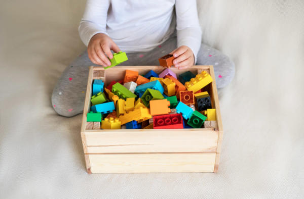 Oyuncak lego bloklarını bir kutuda toplayan çocuk.