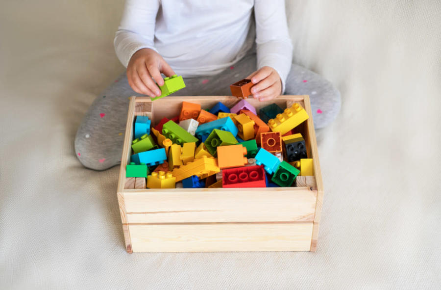 Oyuncak lego bloklarını bir kutuda toplayan çocuk.