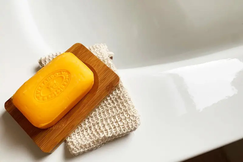 Bir sabun ve lif, ahşap sabunluk üzerinde beyaz lavabo kenarında.