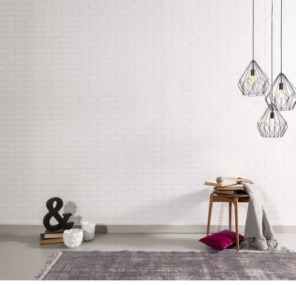 Beyaz tuğla duvara asılı modern avizeler, yanında ahşap sandalye ve üzerinde kitaplar ve battaniye bulunan minimalist bir oda.
