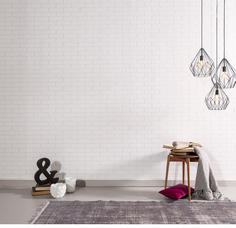 Beyaz tuğla duvara asılı modern avizeler, yanında ahşap sandalye ve üzerinde kitaplar ve battaniye bulunan minimalist bir oda.
