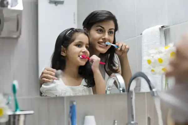 Banyo aynasında dişlerini fırçalayan anne ve kızı.