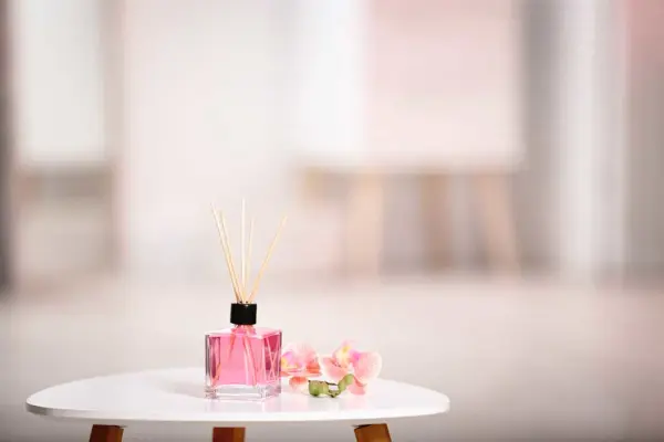 Beyaz bir masanın üzerinde, çubuklu aromatik oda kokusu ve yanında pembe çiçekler.