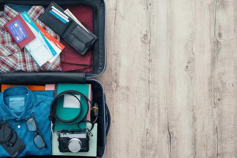 Açık bir bavul, içinde katlanmış giysiler, pasaportlar, cüzdan, kamera ve diğer seyahat eşyaları üzerine ahşap zeminde.