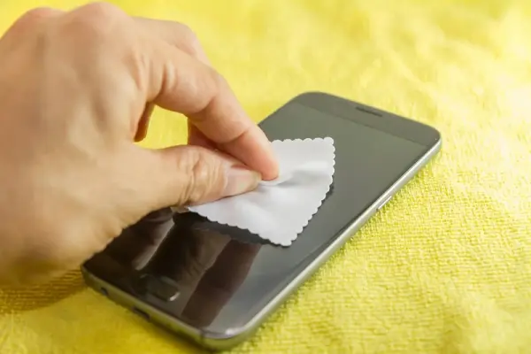 Bir kişinin mikrofiber bezle cep telefonu ekranını temizlediği.