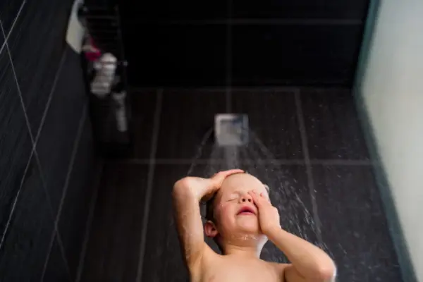 Bir çocuğun duş altında yıkandığı bir banyo sahnesi.