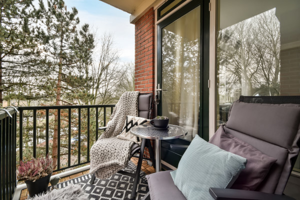 Düzenli ve temiz bir balkon, oturma grubu ve bitkilerle dekore edilmiş.