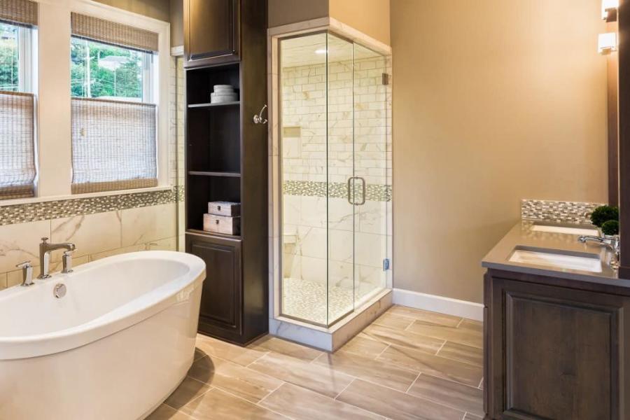 Temiz ve düzenli bir banyo iç mekanı, seramik döşemeler, küvet, cam duş kabini ve lavabo dolabı.