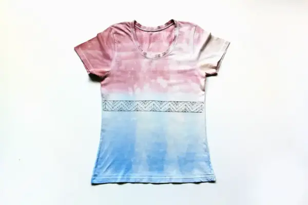 Beyaz zemin üzerine düzgünce serilmiş, pembe ve mavi tie dye desenli bir tişört.