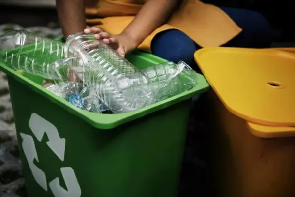 Bir kişi geri dönüşüm kutusuna plastik şişeler atıyor.