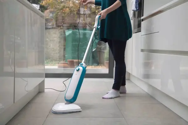 Bir kadın elektrikli süpürge ile yerleri temizliyor.