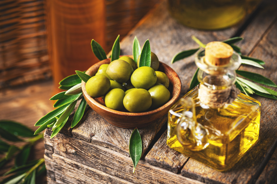 Ahşap yüzeyde zeytin yaprakları ile süslenmiş bir kâse içinde yeşil zeytinler ve yanında zeytinyağı şişesi.