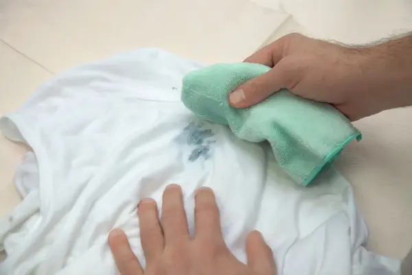 Beyaz tişört üzerindeki lekeyi temizlemeye çalışan bir el.