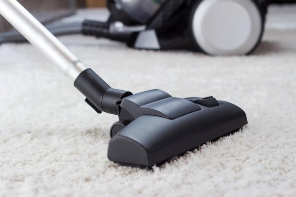 Beyaz halı üzerinde elektrikli süpürge başlığı ve arka planda süpürgenin gövdesi.