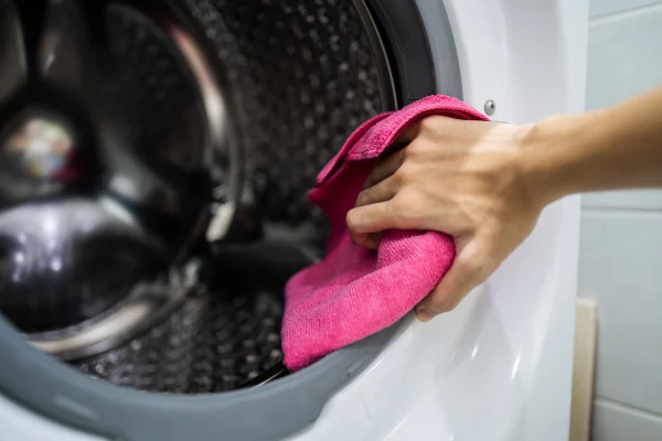 Bir kişi pembe bir bezle çamaşır makinesinin lastiğini silerken.