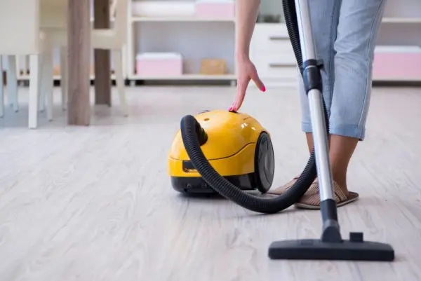 Bir kişi sarı renkli elektrikli süpürgeyi kullanarak temizlik yapıyor.