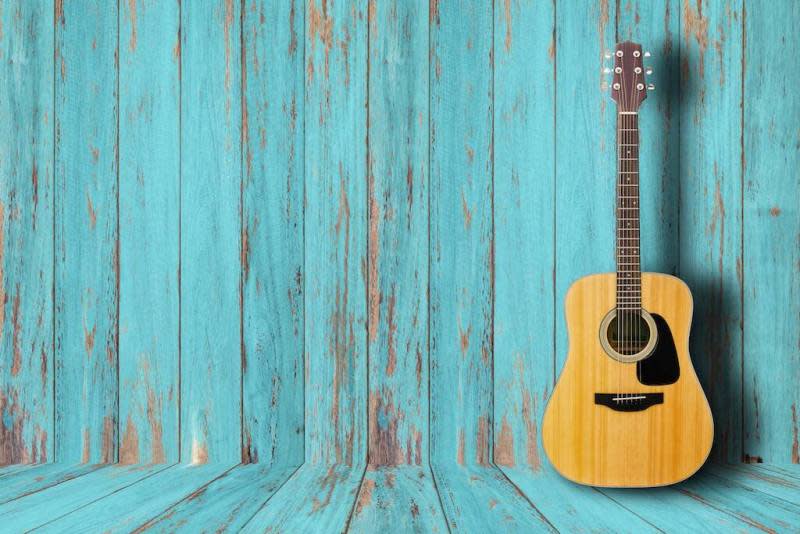 Mavi ahşap duvar önünde duran akustik gitar.
